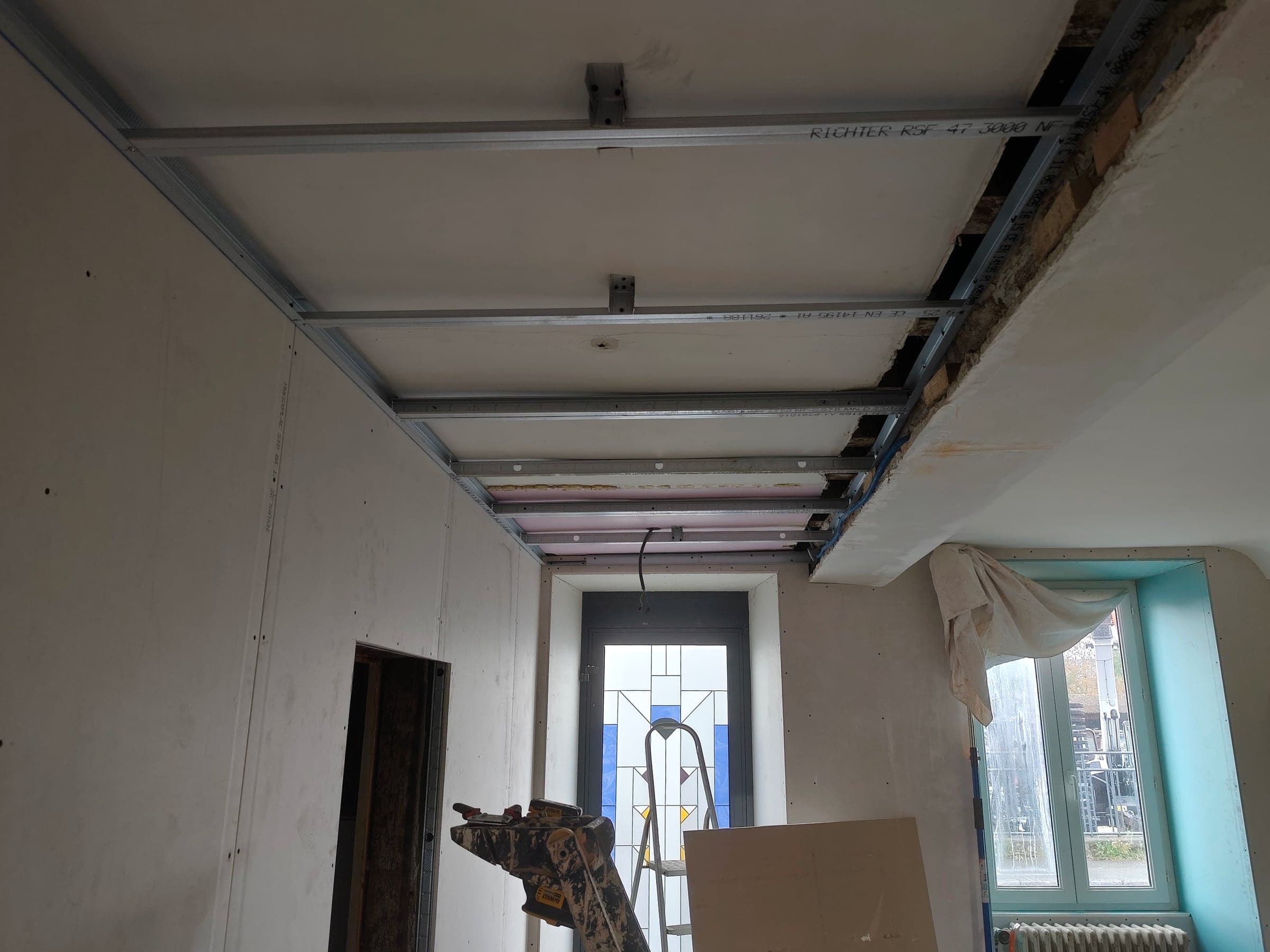 Fourrures métalliques au plafond et murs doublés, porte à vitrail au fond du couloir