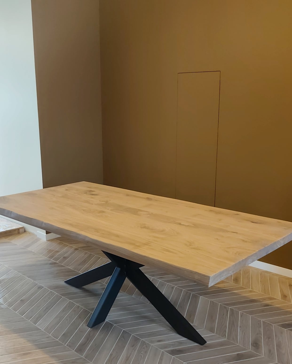 La table en chêne sur un piétement en métal noir, dans une salle à manger au parquet en chevrons
